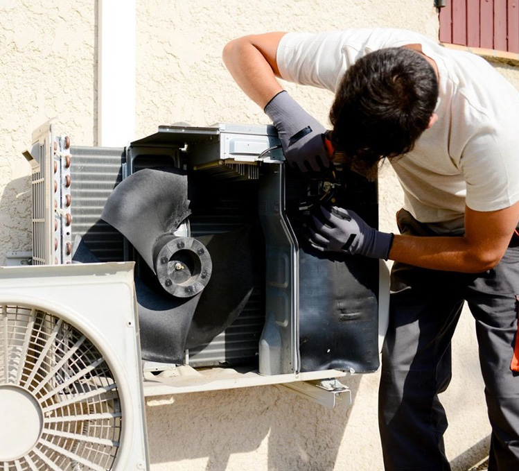 Young man electrician installer working on outdoor compressor unit air conditioner